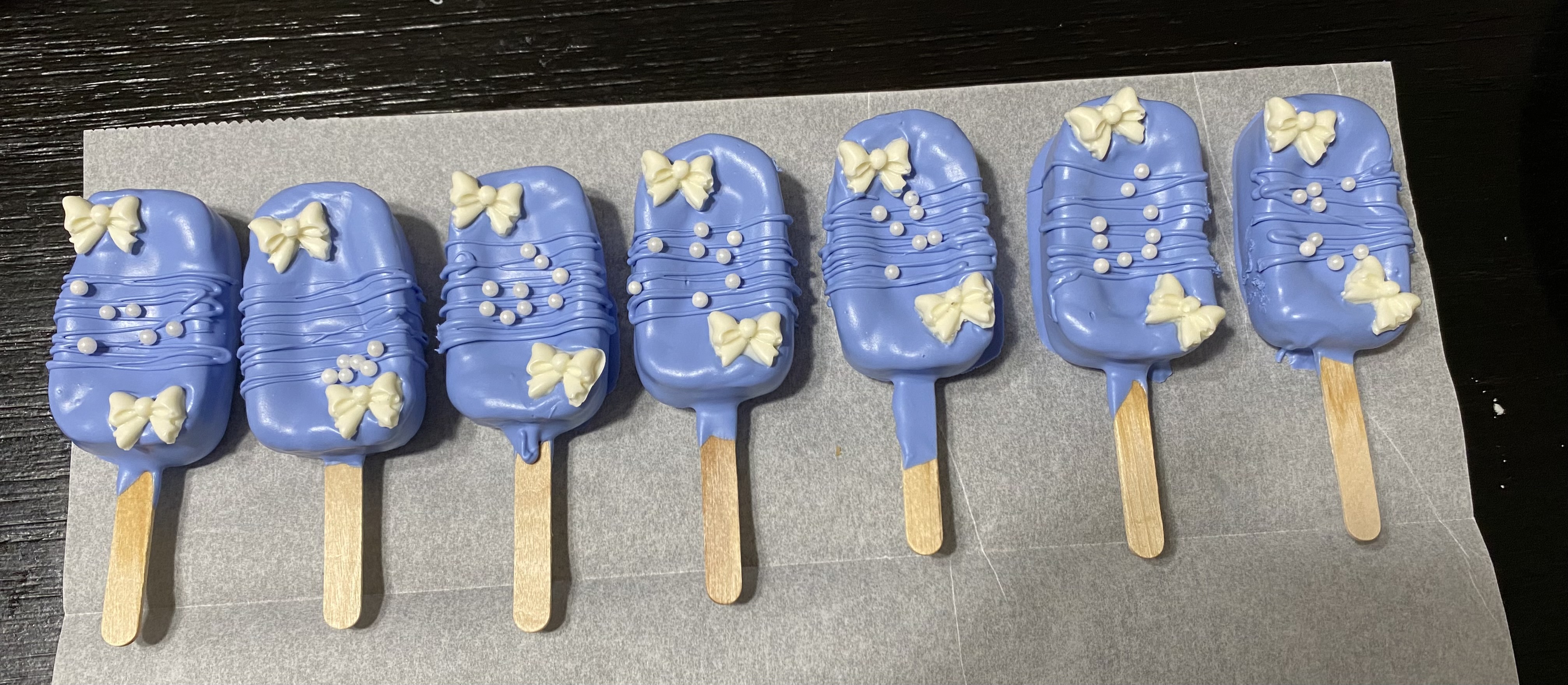 Blue decorated treats on sticks with white bows and sprinkles