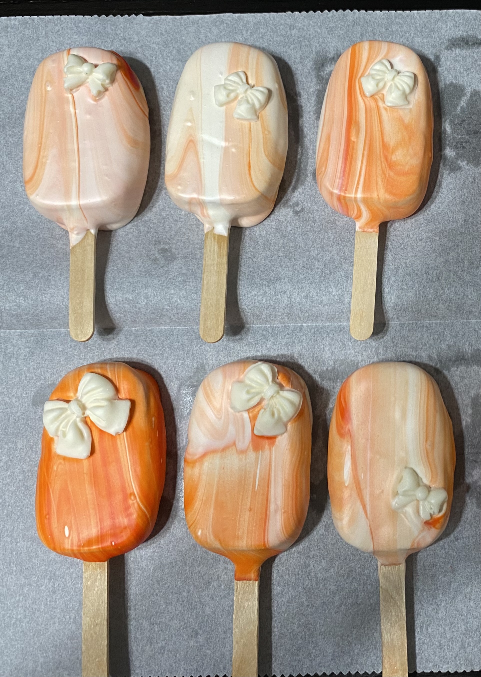 Pastel orange and cream treats on sticks with bow decorations